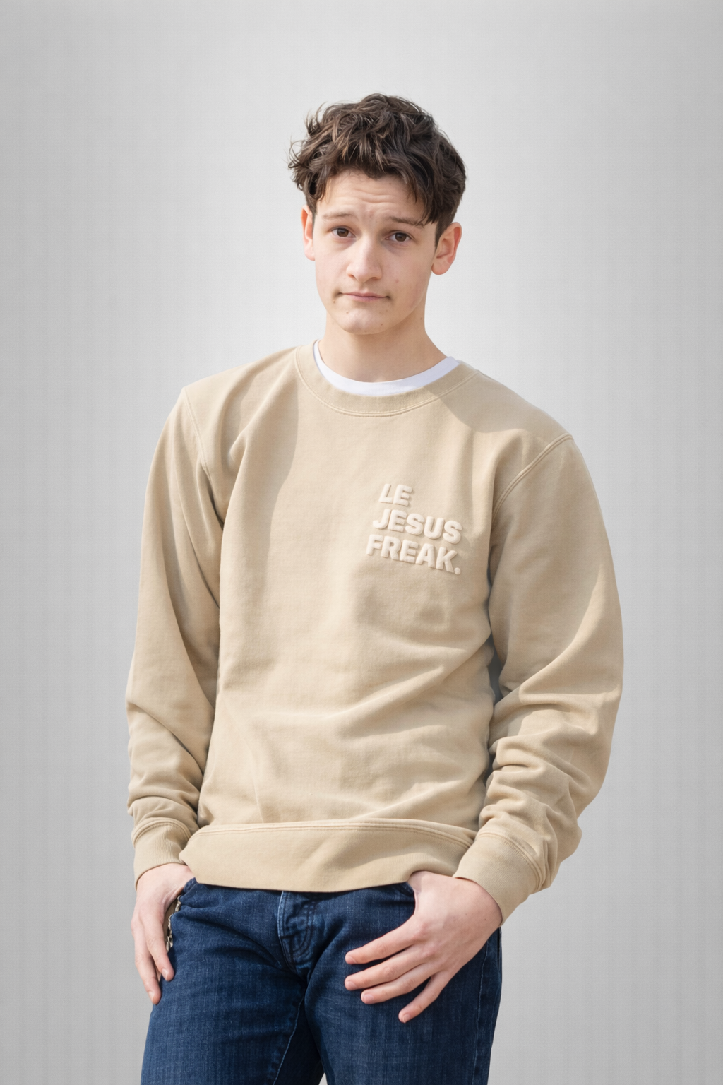 Person wearing a beige sweatshirt with text, standing against a plain background