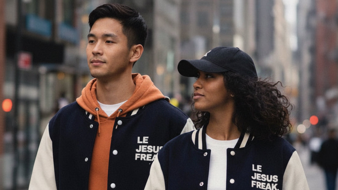 Two people wearing matching 'Le Jesus Freak' letterman jackets on a city street.